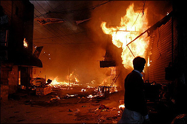 A Pakistani man looks at burning shops after a fire erupted in a shopping center in Lahore. [AFP]