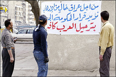 Iraqi men read a newly hung banner asking the new Iraqi government to rid the country of all 'Arabs' along a street in Baghdad. Iraq's new parliament will hold its first session in 10 days, more than a month after the country's historic vote. [AFP]